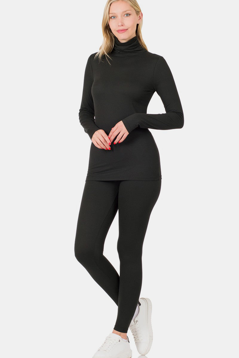 Wearing the Zenana Full Size Turtleneck Top and Leggings Lounge Set in sleek black, along with clean white sneakers, a person stands against a pristine white background.