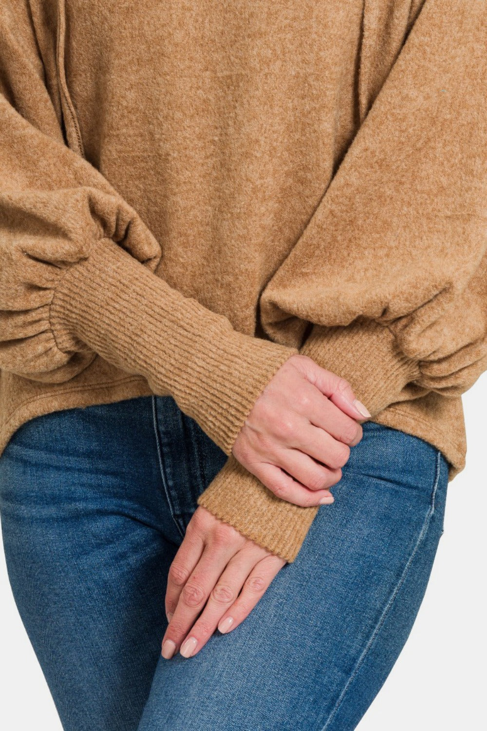 A person wearing a brown Zenana Brushed Hacci Drop Shoulder Cropped Hoodie and blue jeans smiles while posing with one hand in a pocket.