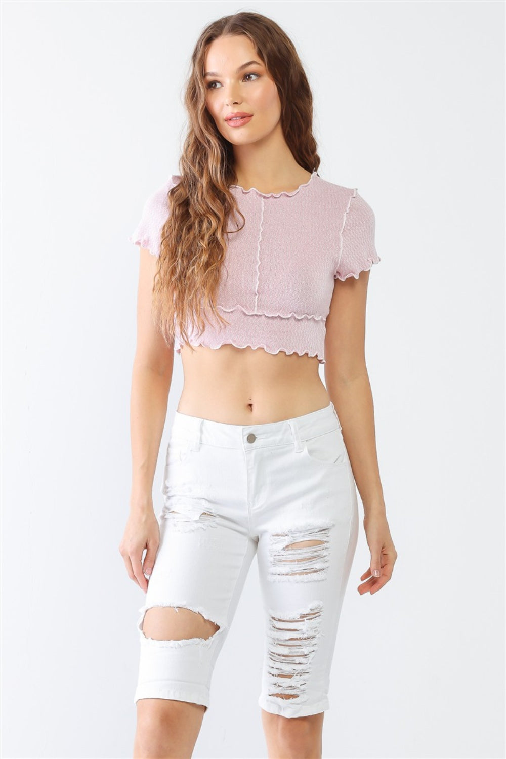 A woman in a lilac crop top and LITZ LA Distressed Bermuda Denim Shorts stands against a plain background, effortlessly channeling a vintage feel.