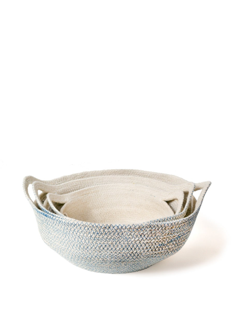 Three round, handwoven blue Amari fruit bowls are nested together. Crafted by Fair Trade artisans, these sustainably handmade pieces add a touch of elegance to any space.