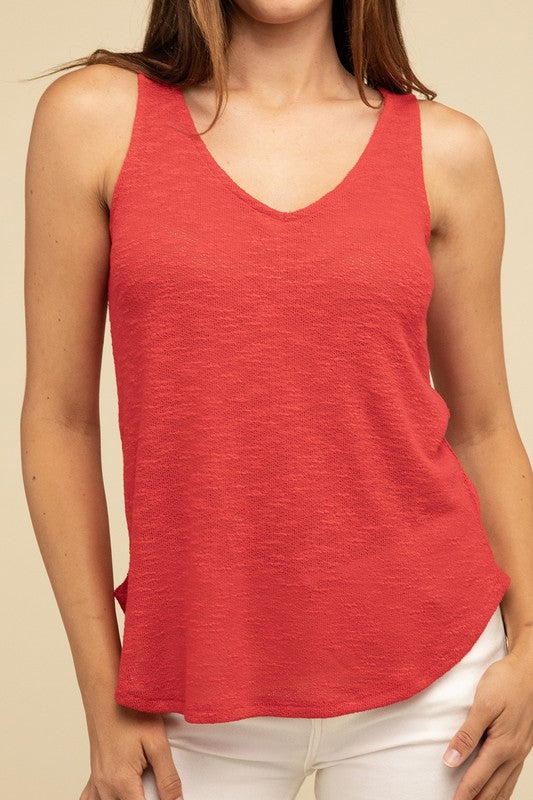 A woman in a stylish and adaptable V Neck Sleeveless Cami Top paired with jeans stands against a beige background. She has long brown hair and maintains a neutral expression.