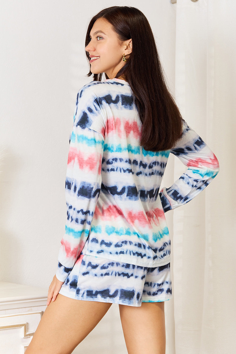 Wearing the Shiny Tie-Dye Dropped Shoulder Lounge Set, this person radiates comfort and style. The vibrant outfit complements the white dresser and curtains in the room perfectly.