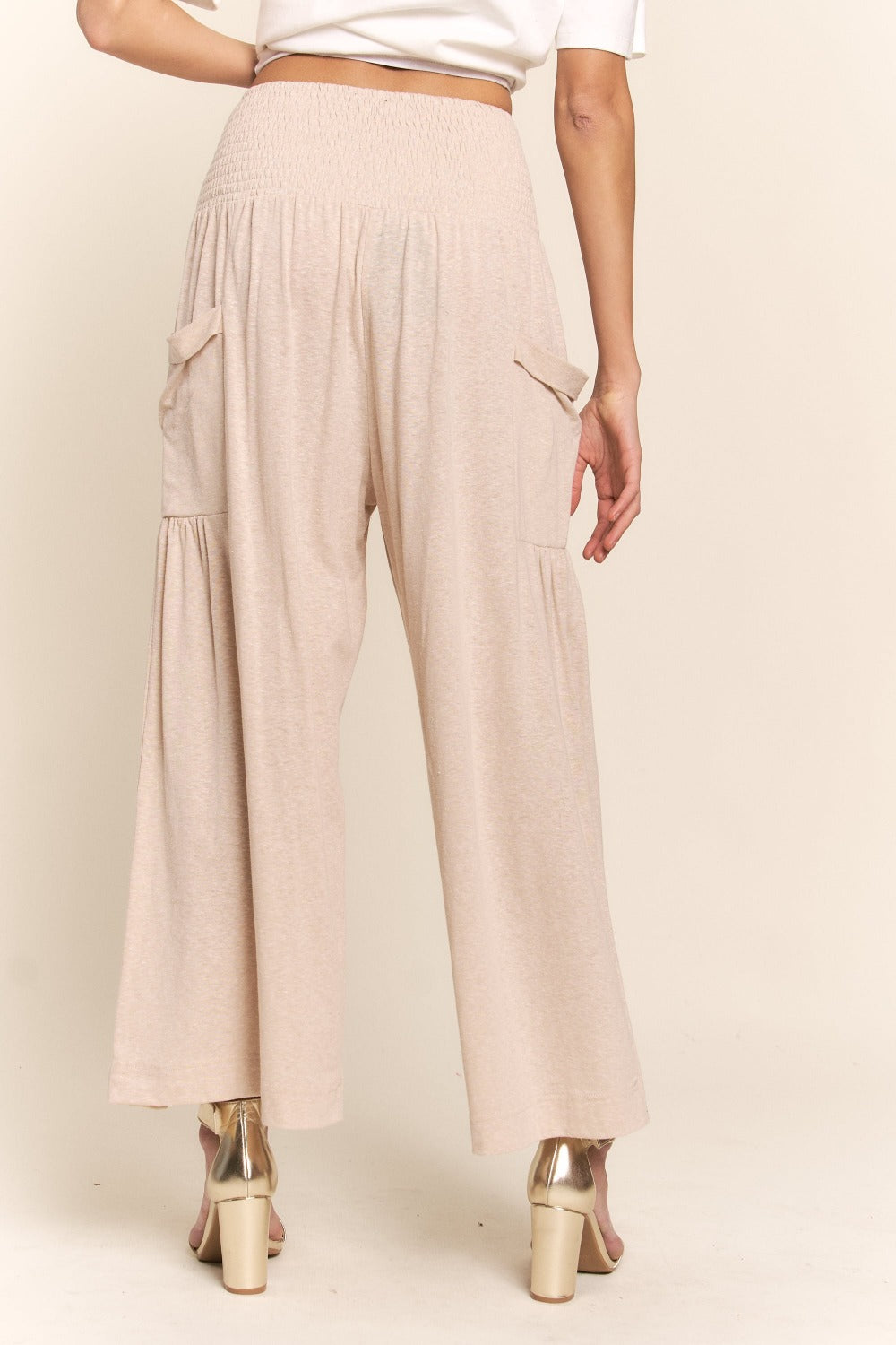 A person wearing J.NNA Smocked Waist Boho Wide Leg Pants with Pockets in beige stands in low-heeled sandals against a plain background, paired with a chic white T-shirt.