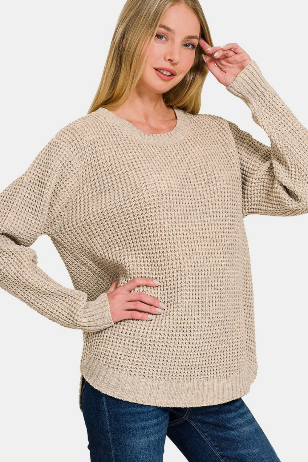 A person wearing a Zenana High Low Long Sleeve Waffle Sweater and blue jeans poses with one hand on their hip.