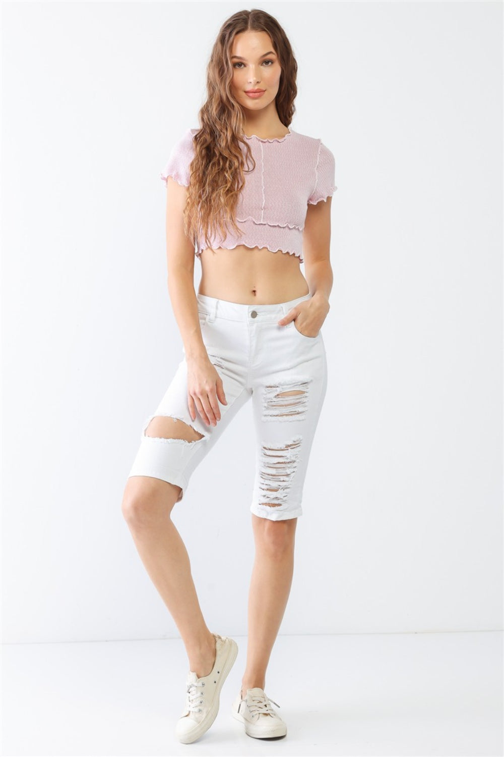 A woman in a lilac crop top and LITZ LA Distressed Bermuda Denim Shorts stands against a plain background, effortlessly channeling a vintage feel.