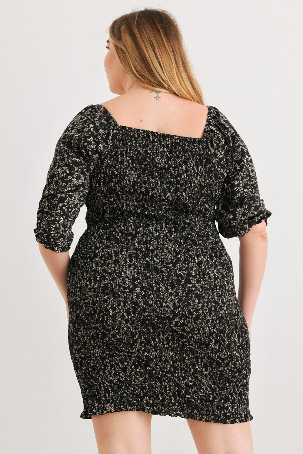 A person poses confidently wearing the Zenobia Plus Size Smocked Printed Square Neck Mini Dress in black and white, paired with black sandals, against a plain white background.