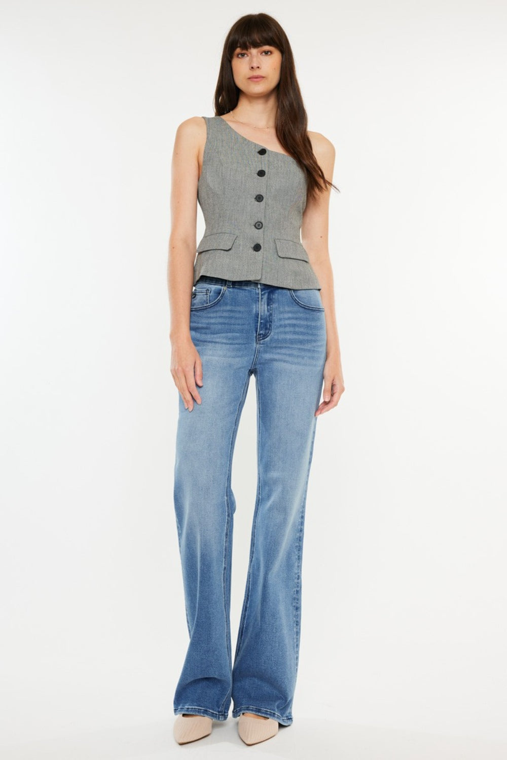 A person stands wearing a sleeveless, buttoned top paired with Kancan Ultra High Rise Cat's Whiskers Jeans. They have long, dark hair and are standing against a plain white background.