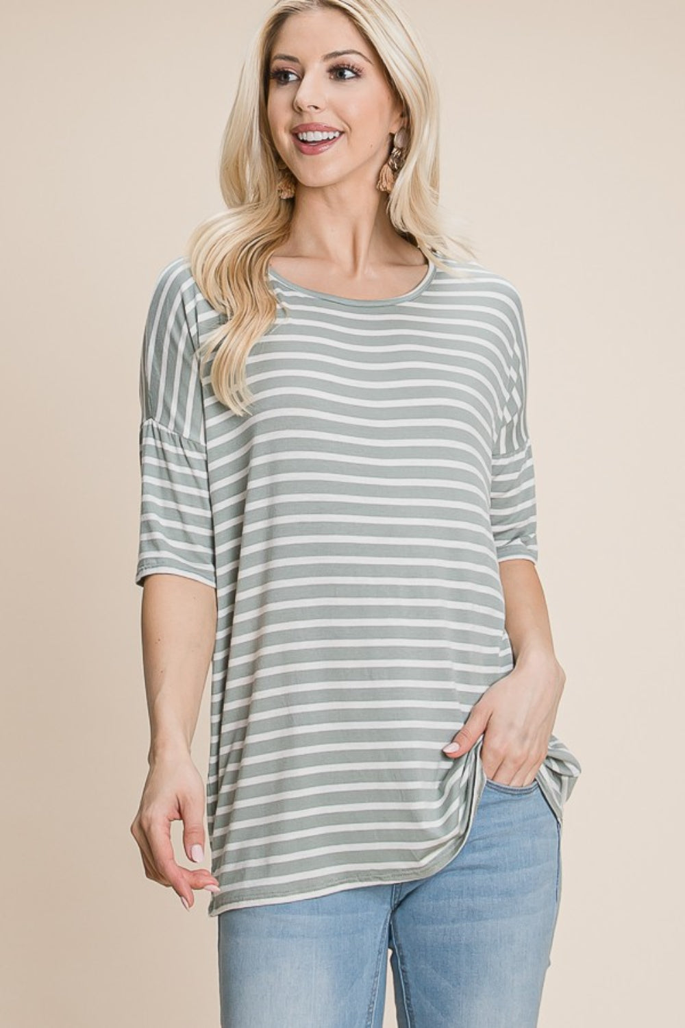 A woman with long blonde hair, dressed in a BOMBOM Striped Round Neck T-Shirt and blue jeans, exudes nautical charm while smiling and looking off to the side.