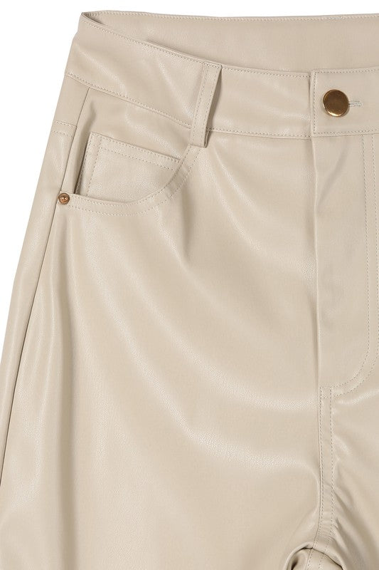 A person wearing a white sweater and black Vegan leather pants with hands in the pockets.