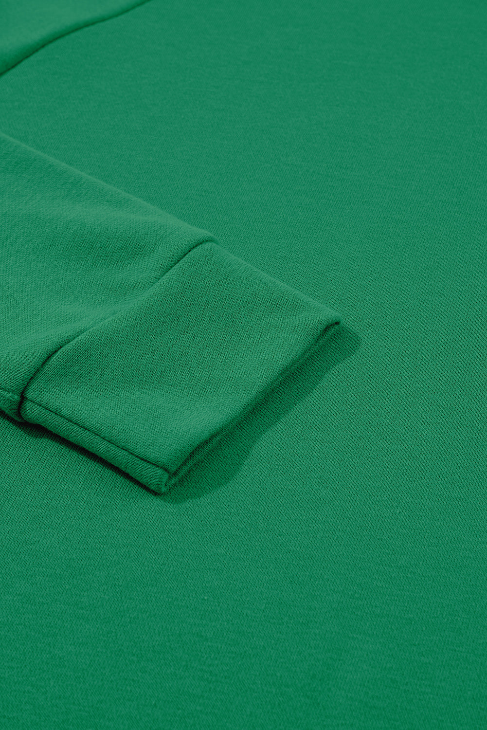 A person with long, light hair is standing with their back to the camera, wearing a comfy Green Solid Round Neck Raglan Sleeve Sweatshirt and blue jeans, against a gray textured wall background.