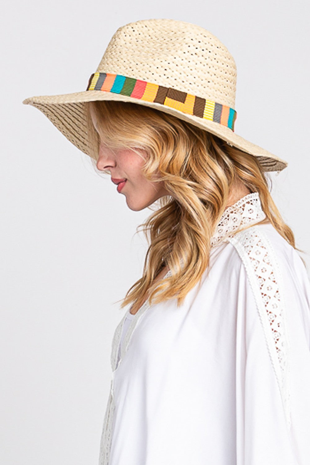 The Fame Contrast Wide Brim Straw Hat, featuring a vibrant multicolor band, is elegantly showcased on a sandy beach background with delicate palm leaf shadows, making it the ideal stylish accessory for sun protection.