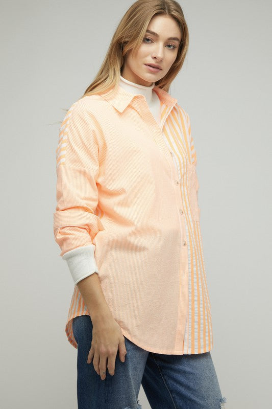 A person wearing a light pink Stripe Button Down Long Sleeve Shirt with rolled-up sleeves and jeans stands with their hands behind their head against a plain background.