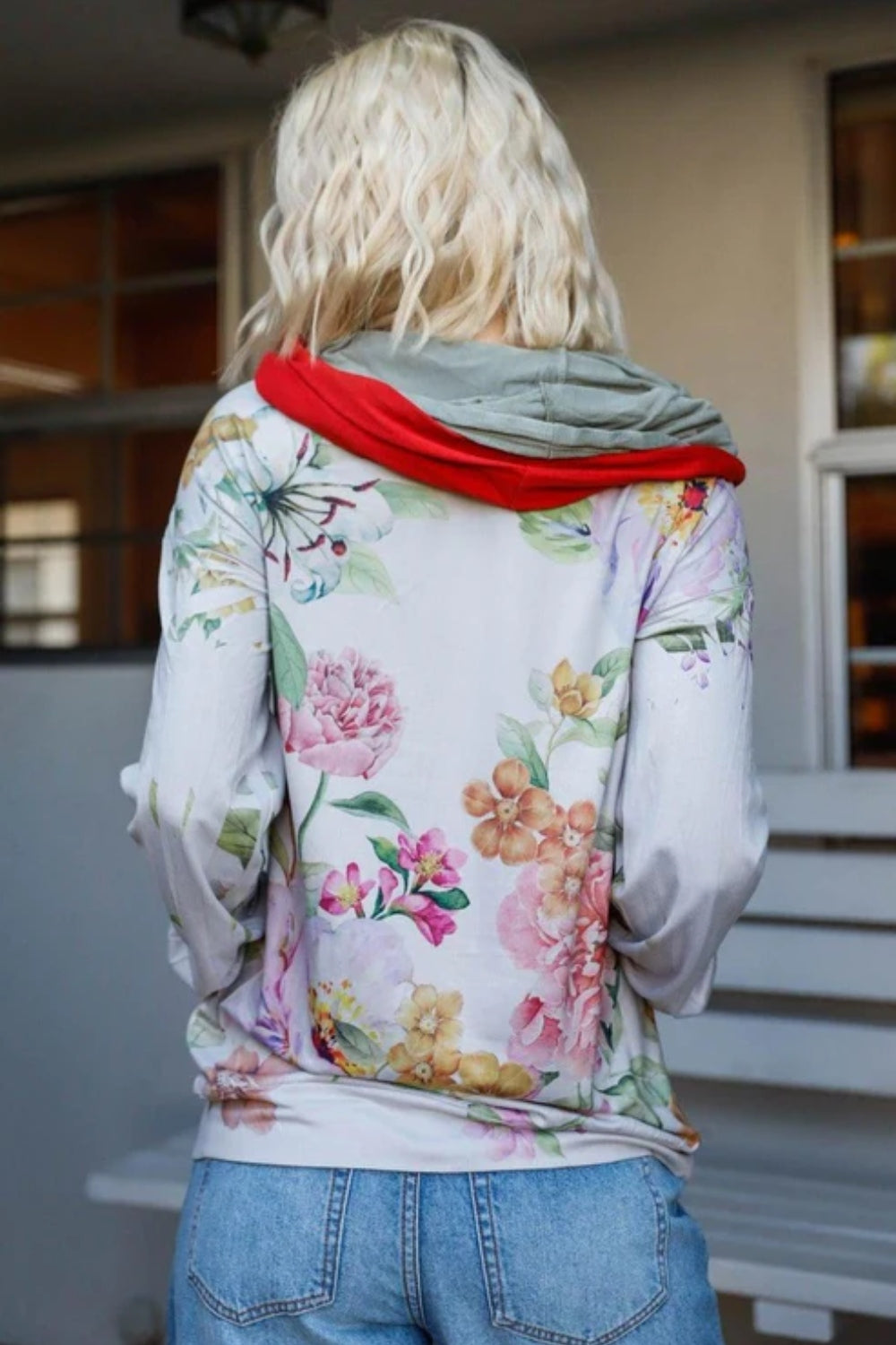 A woman stands outdoors wearing the Blumin Apparel Full Size Floral Zip-Up Hoodie with her hands in the pockets. A leafy green hedge is in the background, adding to the casual chic vibe.