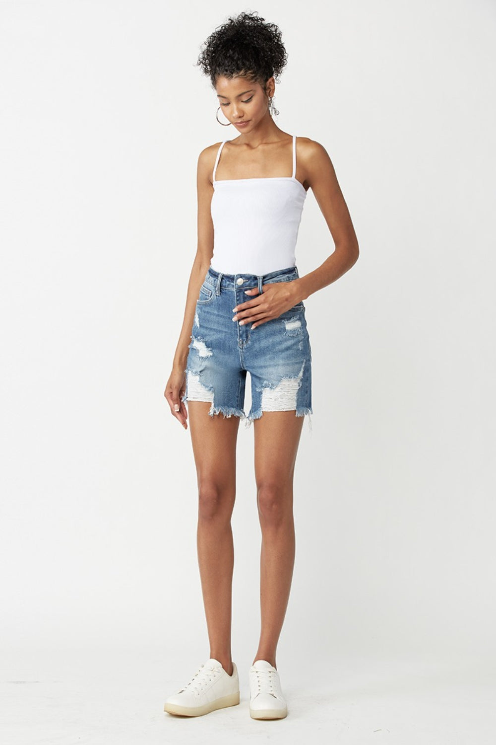 A person wearing RISEN High Waisted Distressed Denim Shorts with frayed detailing and a faded wash. This summer essential embodies an edgy style perfect for warm days.