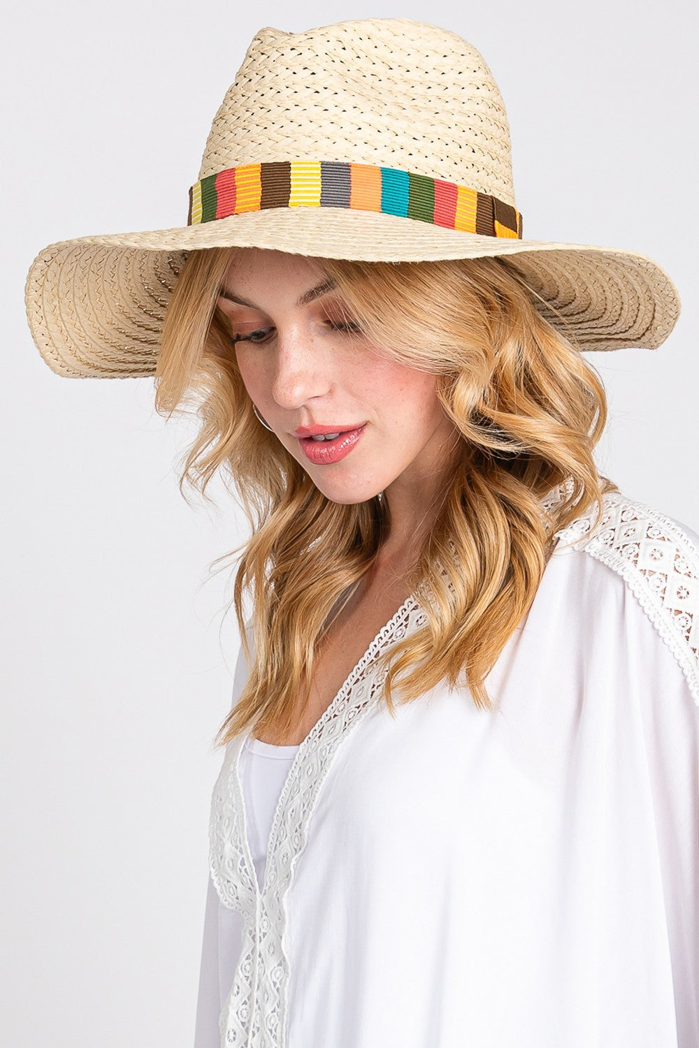 The Fame Contrast Wide Brim Straw Hat, featuring a vibrant multicolor band, is elegantly showcased on a sandy beach background with delicate palm leaf shadows, making it the ideal stylish accessory for sun protection.