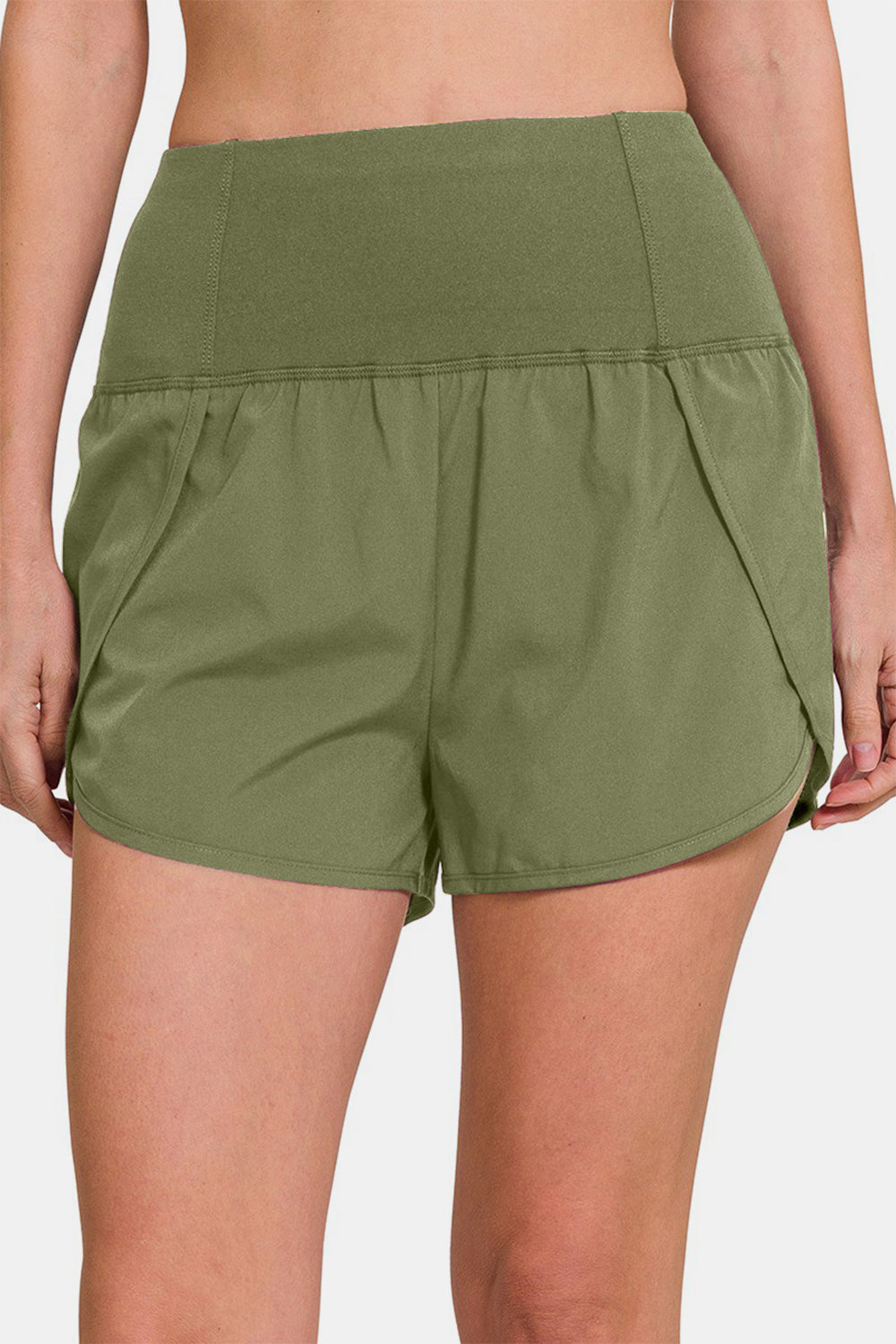 Individual sporting Zenana High-Waisted Zippered Back Pocket Active Shorts in light green, featuring a wide waistband, side slits, and a convenient zippered back pocket—ideal for active wear.