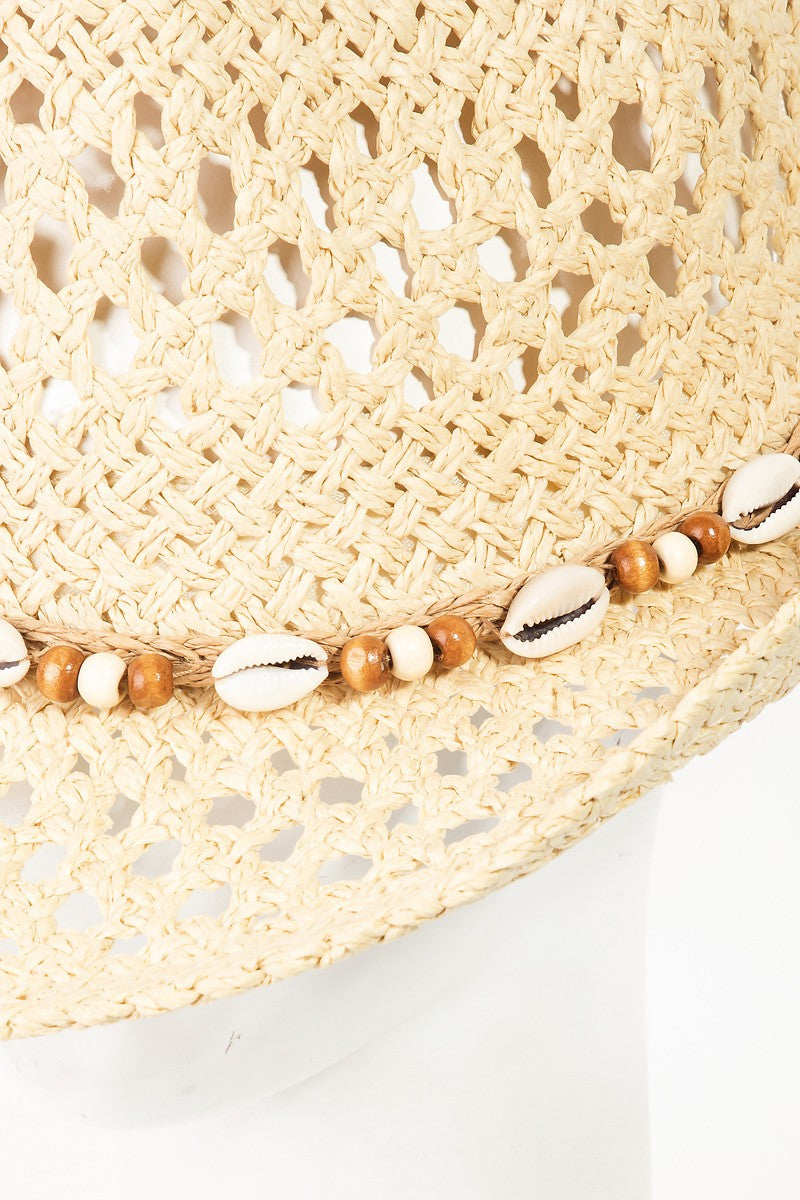 The Fame Cowrie Shell Beaded String Straw Hat, featuring cowrie shells and decorative beads, sits elegantly on a white mannequin head.