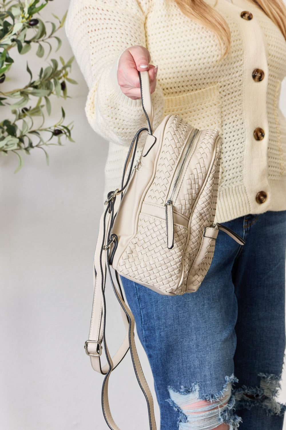 A person wearing a cream sweater and jeans is carrying the SHOMICO PU Leather Woven Backpack in brown.