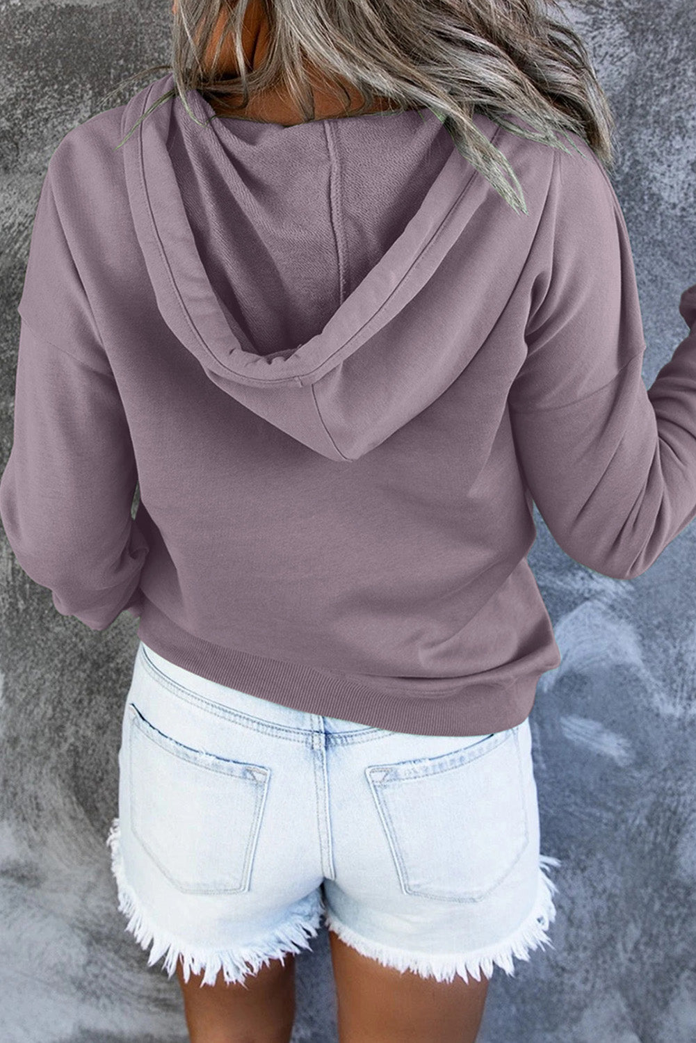 Back view of a person wearing a Purple Snap Button Pullover Hoodie with Pocket and light blue denim shorts with frayed hems, perfect for casual occasions, standing against a grey textured background.