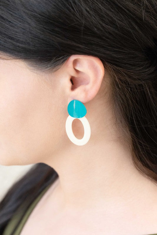 A pair of Bright Color Block Dangle Earrings with teal and white elements on a beige background.