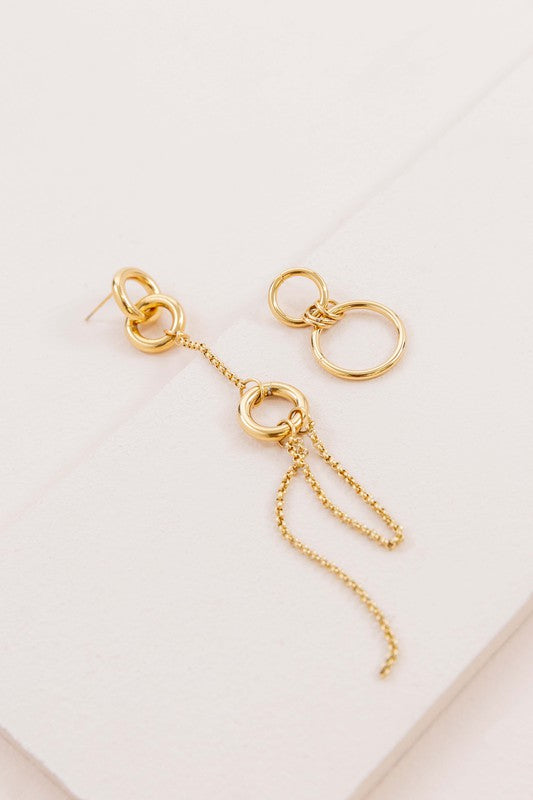 Asymmetrical circle drop earrings with chain and hoop design displayed on a white surface.