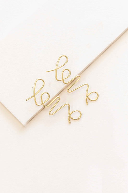 In the Name of Love Earrings wire bent into the word "love" displayed on a white surface next to an envelope.
