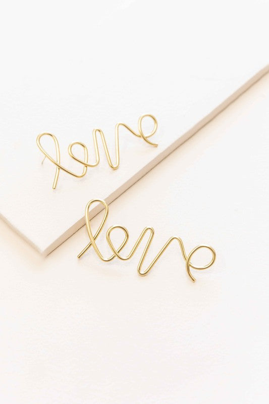 In the Name of Love Earrings wire bent into the word "love" displayed on a white surface next to an envelope.