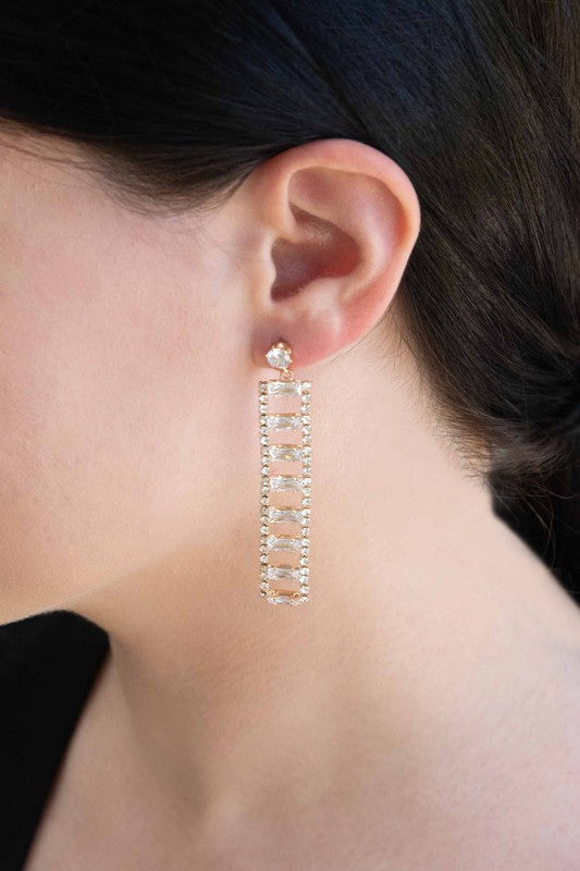 A Dozen Diamonds Dangle Earrings on a pale pink background.