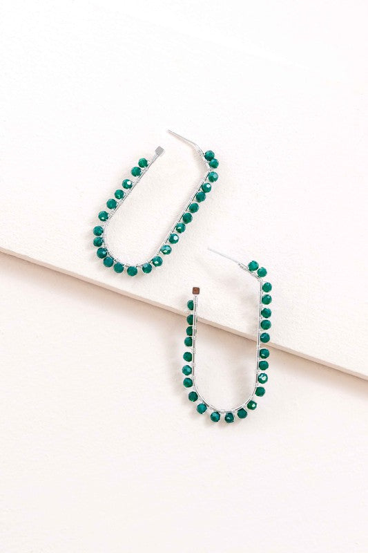 Beaded Racetrack Hoop Earrings featuring gold wire and accented with emerald green beads, displayed on a white surface.