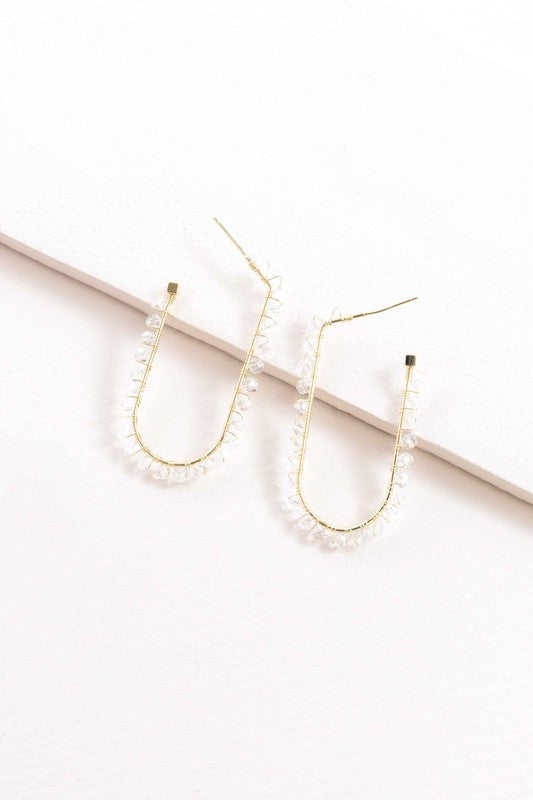 Beaded Racetrack Hoop Earrings featuring gold wire and accented with emerald green beads, displayed on a white surface.