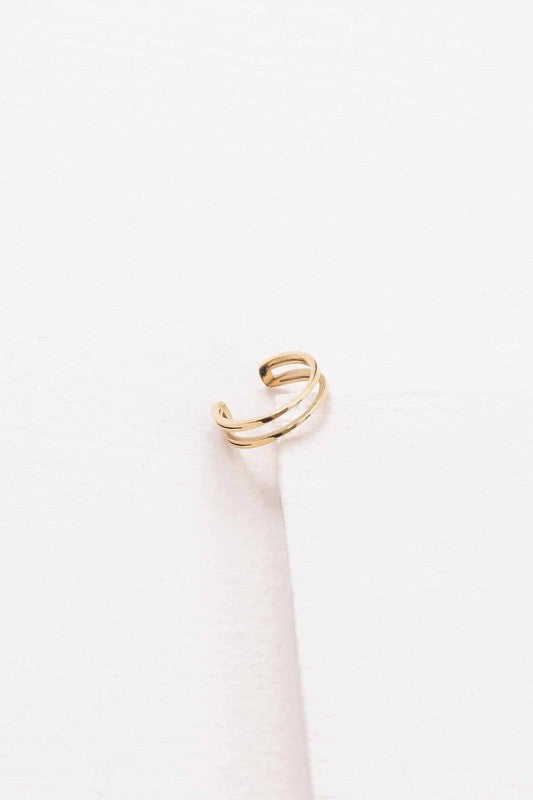 This minimalist jewelry piece, aptly named "Double the Gold Ear Cuff," is crafted from 14K gold over stainless steel and showcases a sleek double band design. Elegantly placed on a white surface, it embodies the simple sophistication of a golden open cuff ring.