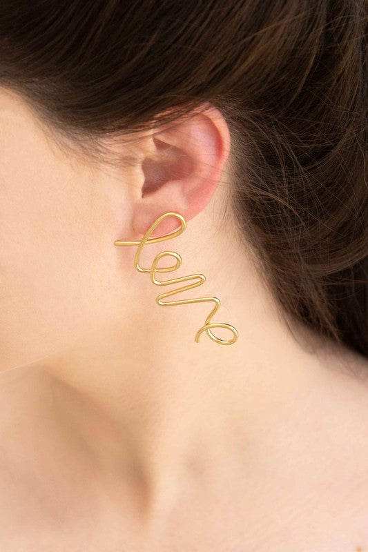 In the Name of Love Earrings wire bent into the word "love" displayed on a white surface next to an envelope.