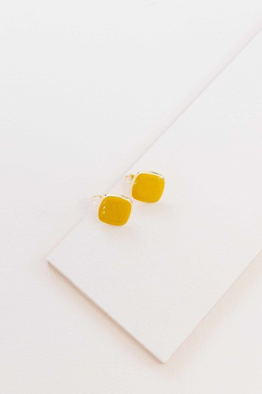 The On the Go Hook Earrings 14K, a pair of square, yellow earrings with 14K gold plate trim, rest on a white surface, bringing a hint of casual style with their elegant yet understated design.