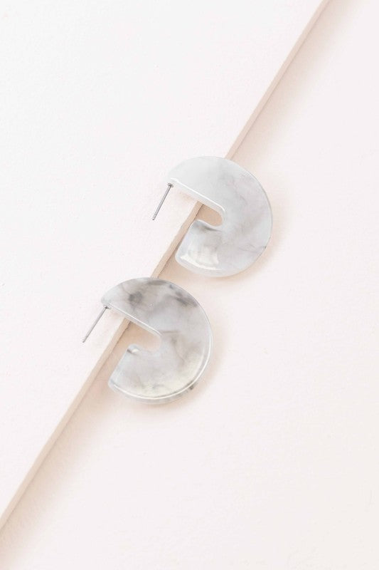 A pair of Marble Half Hoop Earrings displayed against a light pink background.