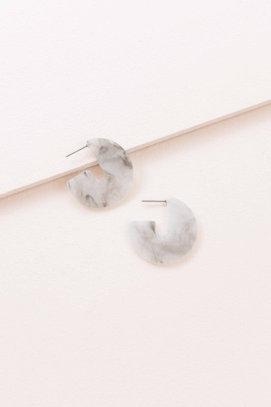 A pair of Marble Half Hoop Earrings displayed against a light pink background.