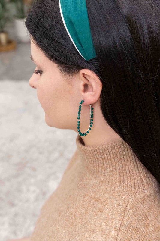 Beaded Racetrack Hoop Earrings featuring gold wire and accented with emerald green beads, displayed on a white surface.