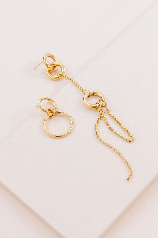Asymmetrical circle drop earrings with chain and hoop design displayed on a white surface.