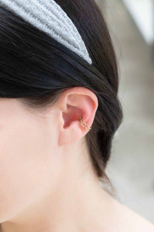 This minimalist jewelry piece, aptly named "Double the Gold Ear Cuff," is crafted from 14K gold over stainless steel and showcases a sleek double band design. Elegantly placed on a white surface, it embodies the simple sophistication of a golden open cuff ring.