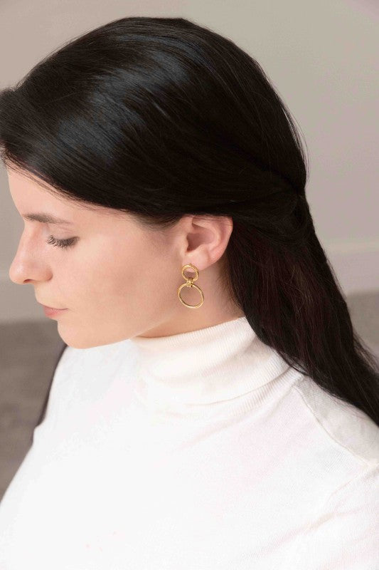 Asymmetrical circle drop earrings with chain and hoop design displayed on a white surface.
