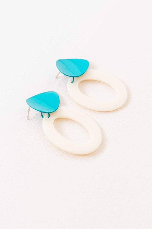 A pair of Bright Color Block Dangle Earrings with teal and white elements on a beige background.