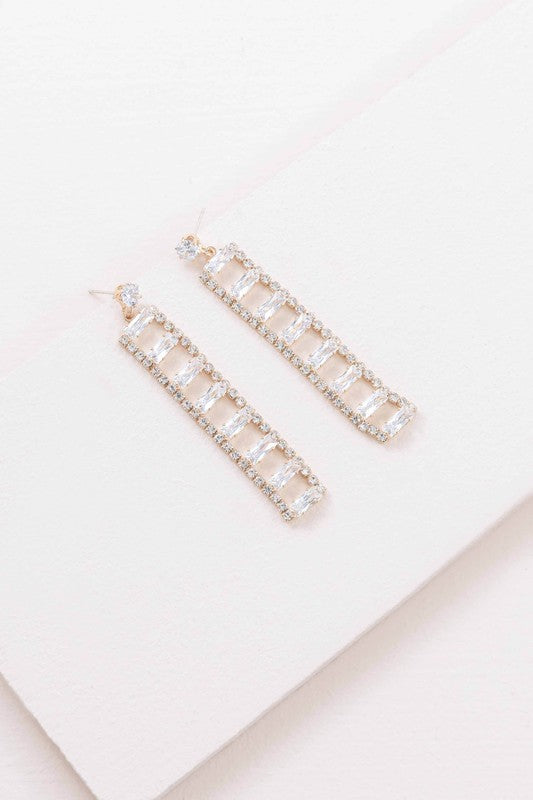 A Dozen Diamonds Dangle Earrings on a pale pink background.