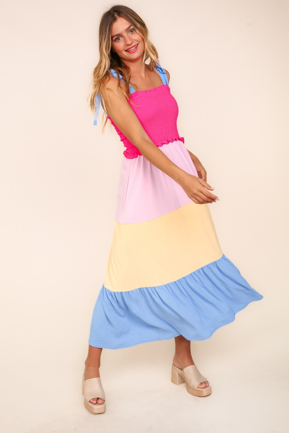 A woman wearing the Haptics Smocked Color Block Tiered Cami Dress in vibrant pink, yellow, and blue, paired with beige platform sandals.