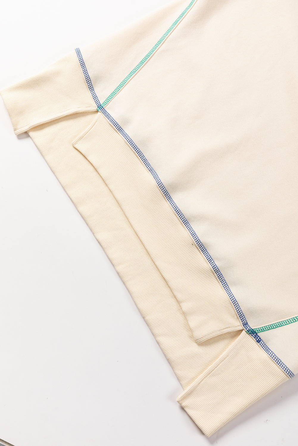 A woman with blonde hair is facing away, wearing a Contrast Stitching Split Baggy Sweatshirt. She stands in a room adorned with plants and wooden furniture in the background.