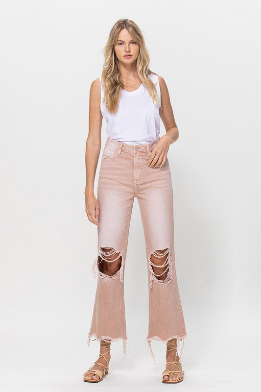 Person wearing 90's Vintage Crop Flare Jeans in rose pink with high waist, distressed details, rips on the knees, and frayed hems, paired with beige strappy sandals.