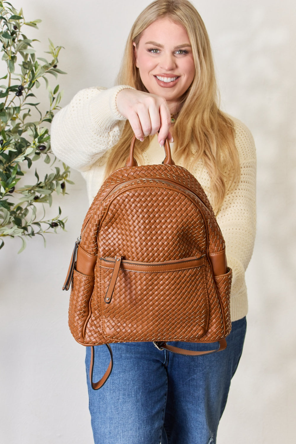 A person wearing a cream sweater and blue jeans carries the SHOMICO PU Leather Woven Backpack, showcasing exquisite craftsmanship with its woven design.