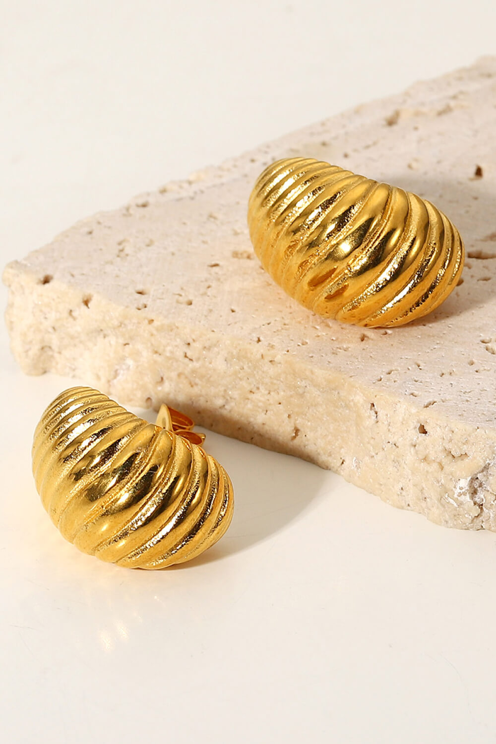 A pair of Shell Shore Spiral Stud Earrings, gold-plated with a ribbed, crescent shape and post-butterfly clasps on a white background.