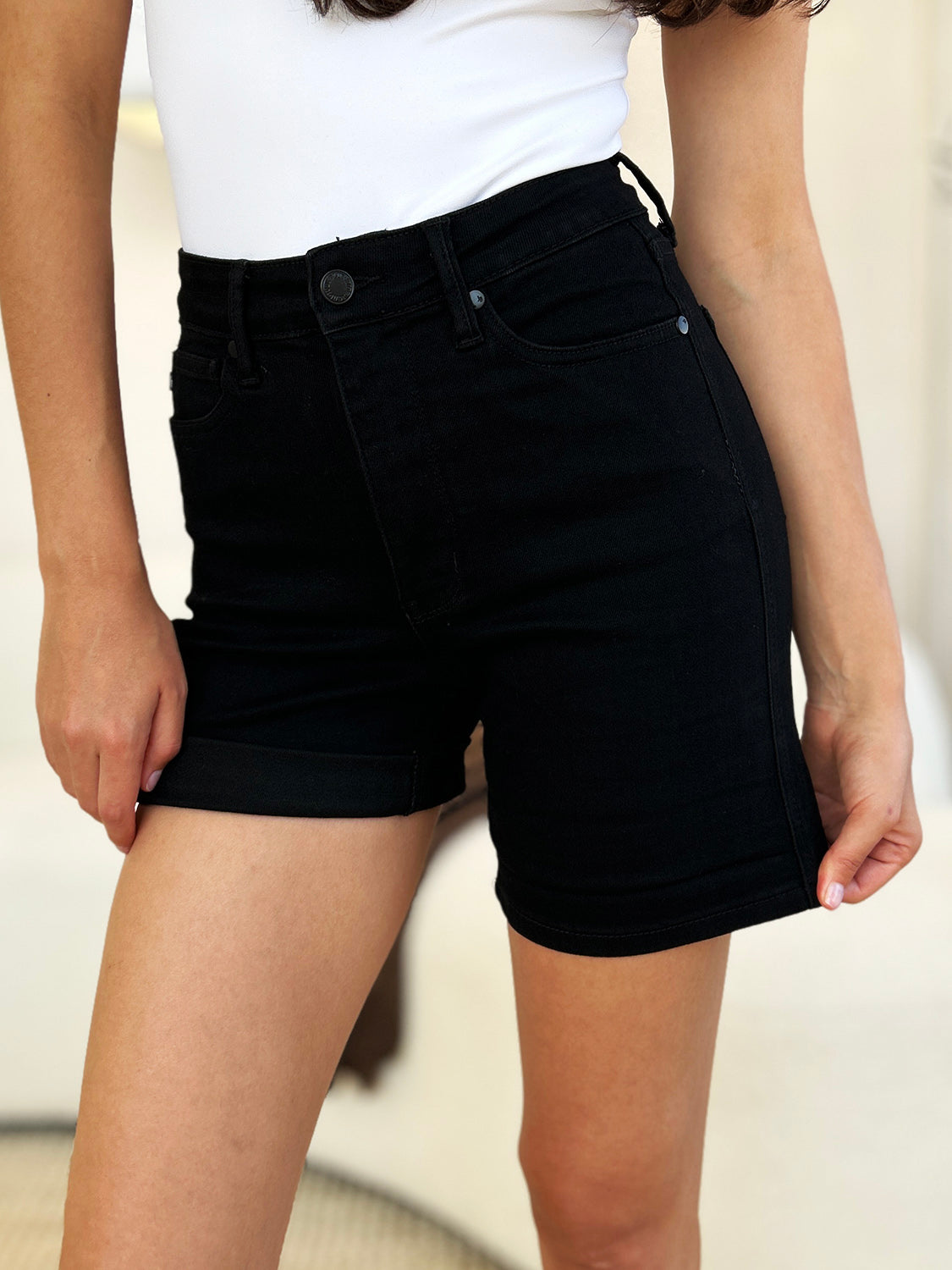 Person wearing a white top and Judy Blue Full Size High Waist Tummy Control Cuffed Denim Shorts, one hand in pocket.