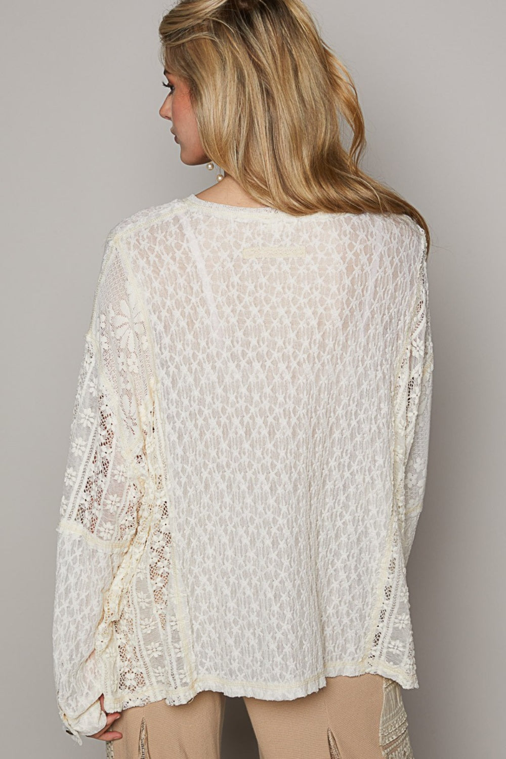 A woman is wearing the POL Round Neck Long Sleeve Raw Edge Lace Top, paired with beige pants, as she stands against a neutral background.