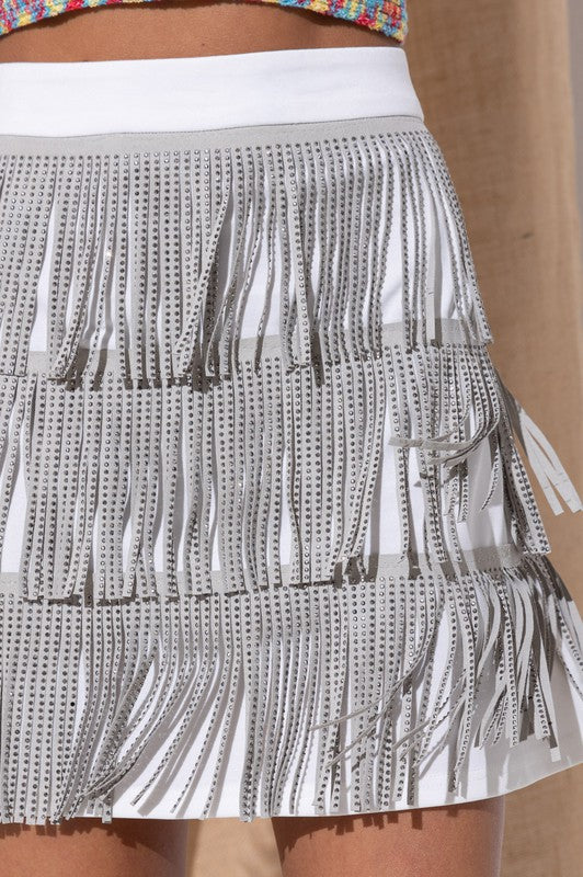 Close-up of the RHINESTONE SUEDE FRINGE SKIRT in pink, featuring a person’s hand resting lightly on the skirt adorned with rhinestone fringes.