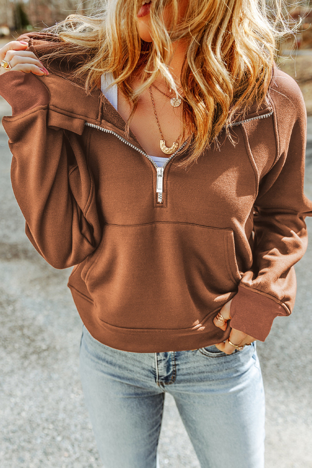 A person with long hair is walking away wearing a Brown Quarter Zip Kangaroo Pocket Hoodie and light blue ripped jeans. The background shows an outdoor setting.